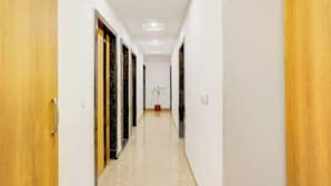 Un pasillo con puertas de madera, paredes blancas y piso de baldosas.