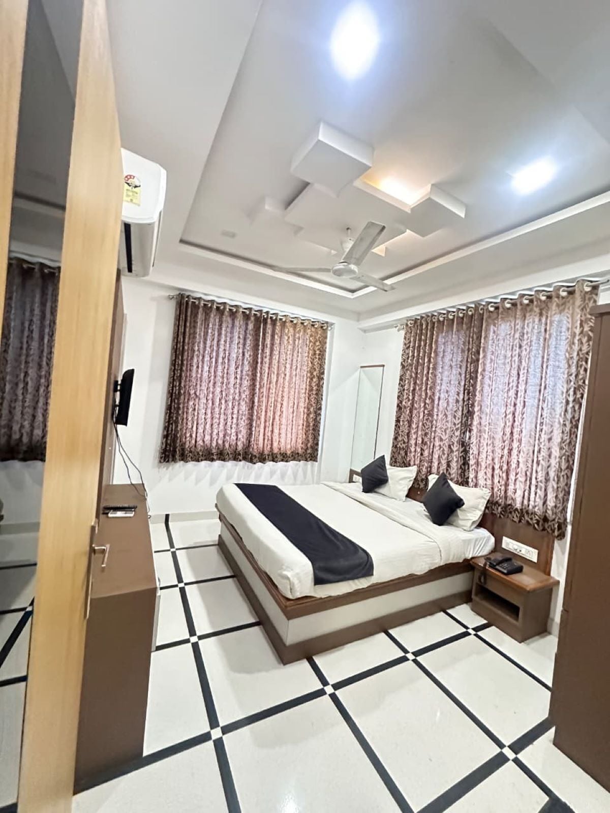 A hotel room with a bed, curtains, a ceiling fan, and a tiled floor.