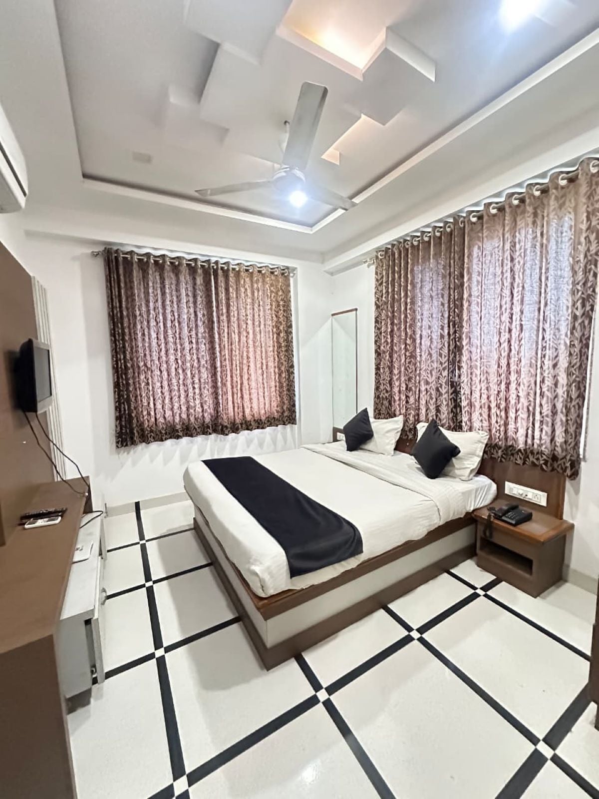 A hotel room with a bed, a nightstand, a mirror, and a ceiling fan.