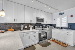 A modern kitchen with white cabinets, a microwave, a stove, and a toaster. - Coastal Relaxation! Amazing Views! Pool, Beach Gear and FREE Parking! ~ 510 Gulf Shores (Indian Shores)