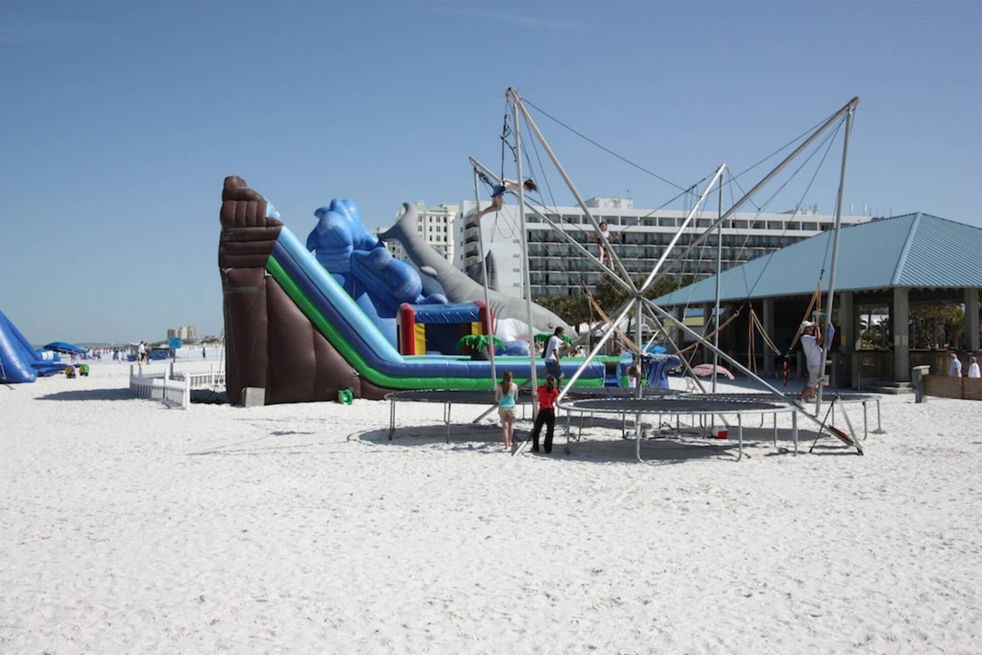 Un parque acuático inflable con toboganes y estructuras para escalar sobre una playa arenosa.