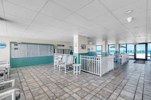 A spacious indoor area with a tiled floor, a row of lockers, and a seating area with chairs and tables. - Coastal Relaxation! Amazing Views! Pool, Beach Gear and FREE Parking! ~ 510 Gulf Shores (Indian Shores)