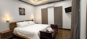 A hotel room with a bed, bedside table, wall-mounted TV, and a large window with curtains.