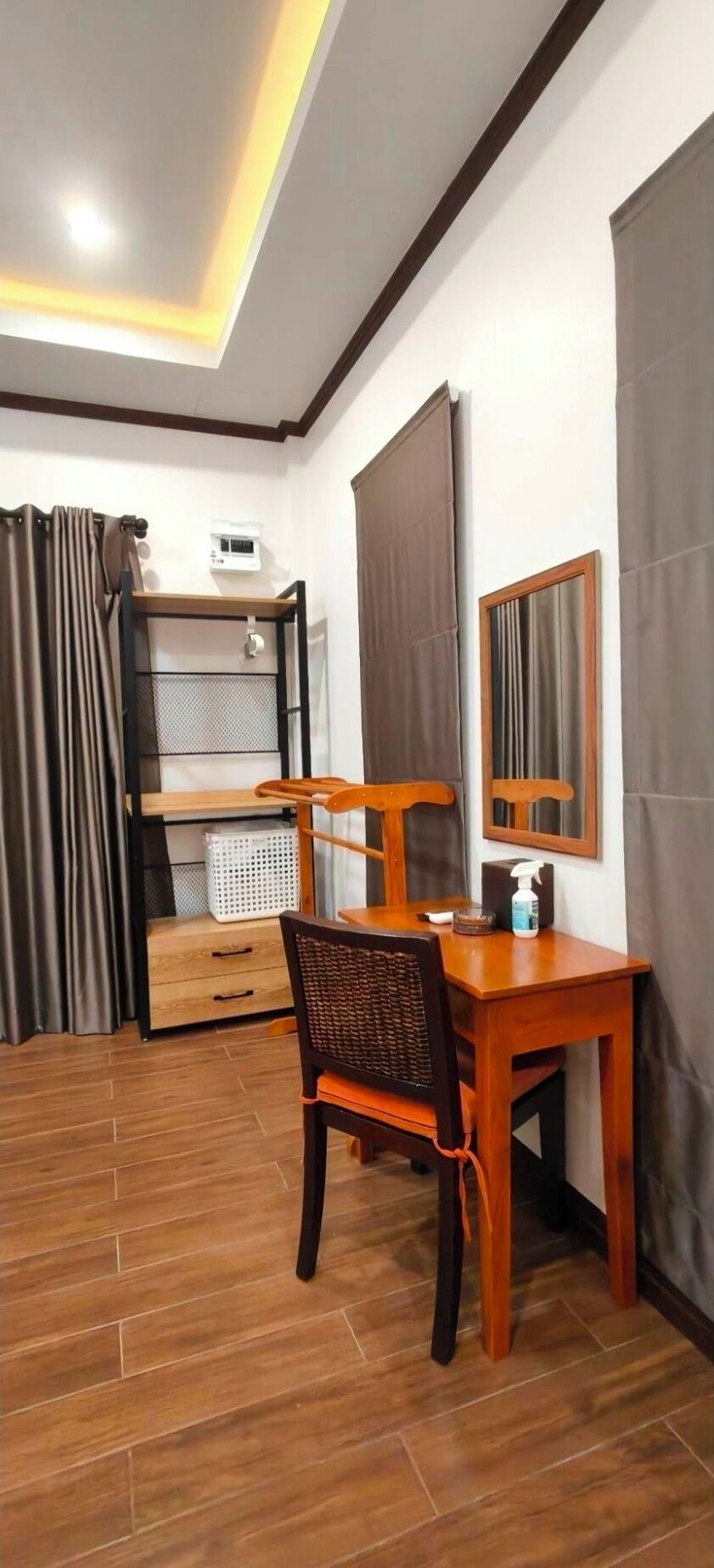 A room with a wooden desk, a chair, a bed with a headboard, a window with curtains, and a ceiling light fixture.