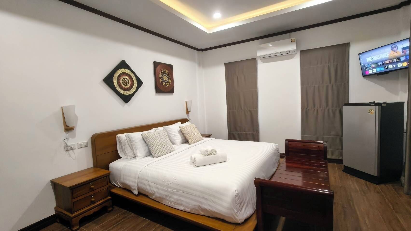 A hotel room with a bed, bedside tables, a TV, and a refrigerator.
