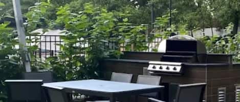 An outdoor patio with a table and chairs, a grill, and a brick wall.