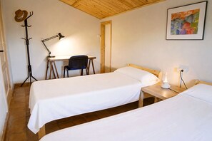 Una habitación con dos camas individuales, un escritorio con una silla, un perchero y una lámpara.