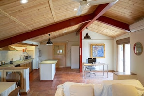 A spacious loft with a high ceiling, a kitchen area, a dining table with a computer, and a large window.