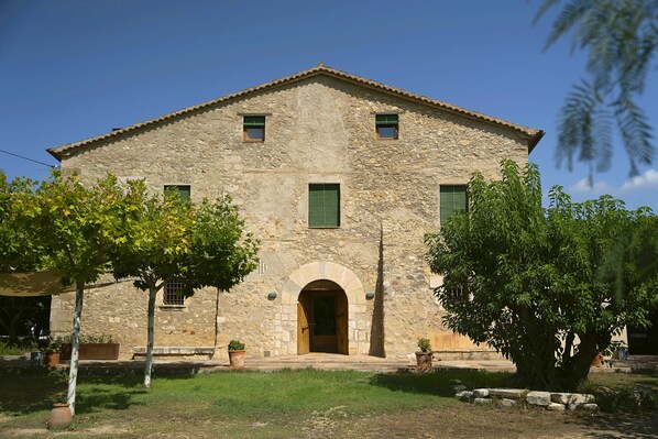A stone building with a central archway, two windows with shutters, and a small door.