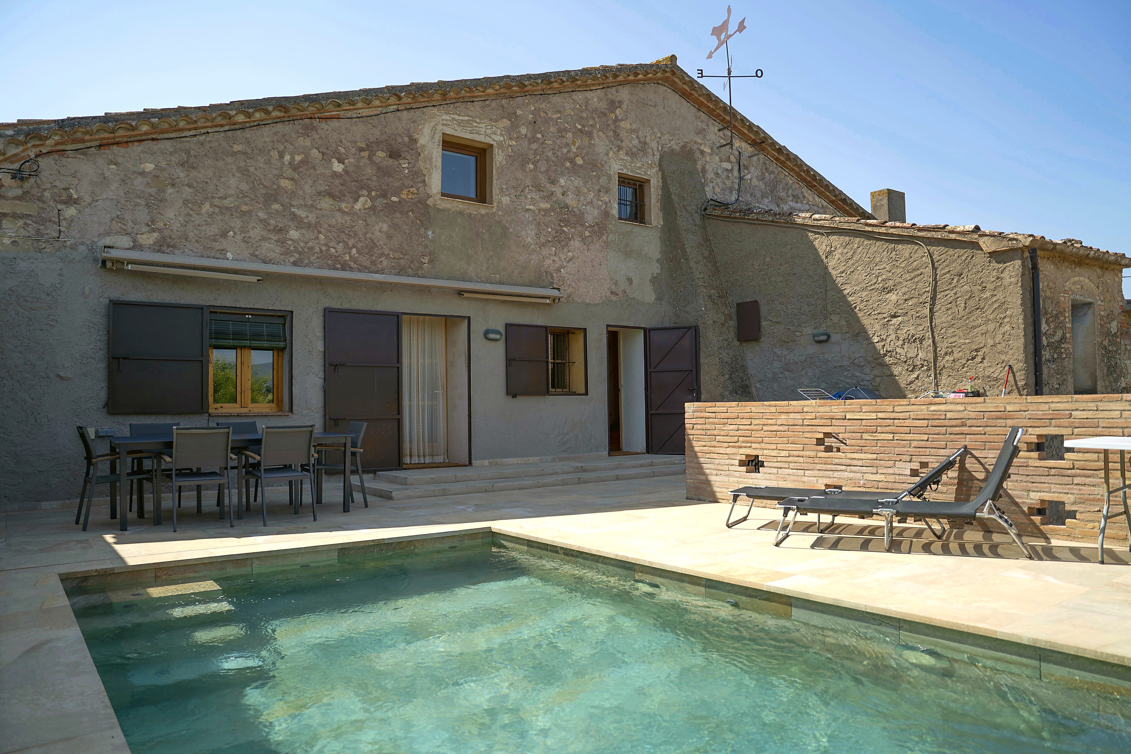 A building with a pool, outdoor seating, and a brick wall.