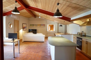 Una habitación amplia con una cama grande, un escritorio con computadora y una kitchenette.