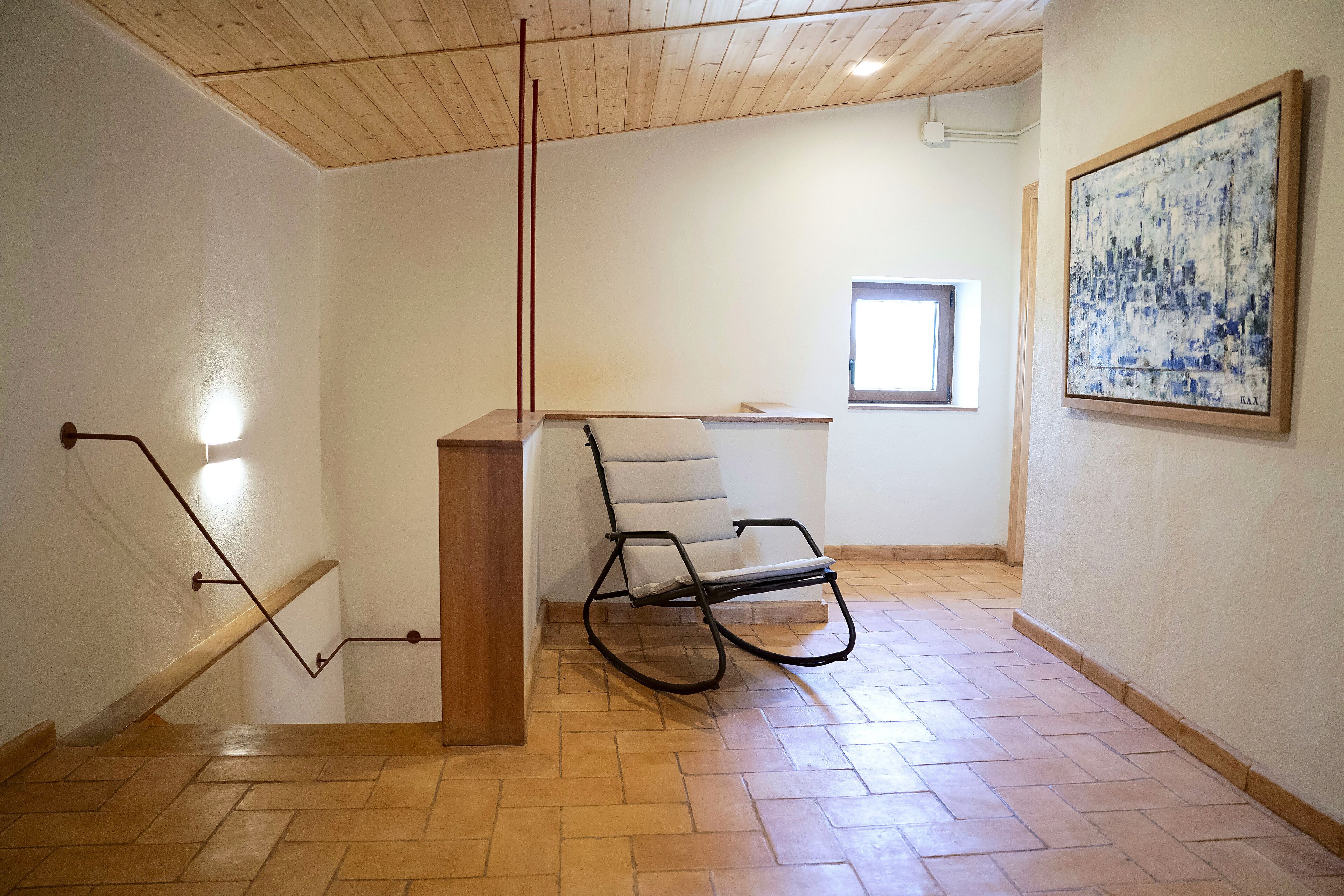 A room with a wooden floor, a chair, a wooden desk, a window, and a painting on the wall.