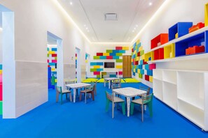 Una habitación luminosa con paredes de bloques de colores, un televisor y mesas con sillas.