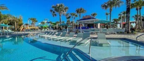 Una piscina cristalina con sillas de descanso, palmeras y un edificio al fondo.