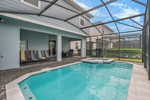 A pool area with a hot tub, lounge chairs, and a covered patio. - Themed 7BR by Disney | Heated Pool + Game Room (Davenport)