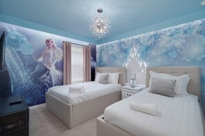 A hotel room with a large mural, two beds, a chandelier, and a nightstand. - Themed 7BR by Disney | Heated Pool + Game Room (Davenport)