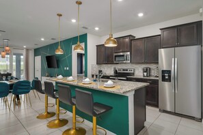 A modern kitchen with a central island, stainless steel appliances, and pendant lighting. - Themed 7BR by Disney | Heated Pool + Game Room (Davenport)