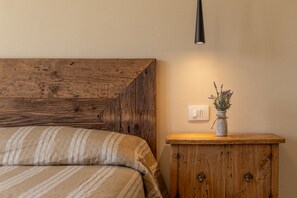 A bedroom with a bed, a wooden headboard, a bedside table with a vase of flowers, and a wall-mounted light fixture. - APPARTAMENTI IL SENTIERO DEL GRANITO - GRANITO BILO 1 DX (Campo nell'Elba)