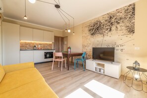 A modern living room with a yellow sofa, a dining area with a table and chairs, a kitchen with white cabinets, and a large map on the wall. - APPARTAMENTI IL SENTIERO DEL GRANITO - GRANITO BILO 1 DX (Campo nell'Elba)