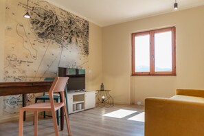 A room with a large map on the wall, a dining table with chairs, a sofa, and a window. - APPARTAMENTI IL SENTIERO DEL GRANITO - GRANITO BILO 1 DX (Campo nell'Elba)