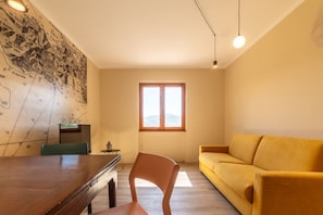 Una stanza con un tavolo da pranzo in legno, un divano giallo, una mappa appesa al muro e una finestra con vista.