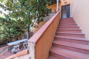 A staircase with red steps leading to a door, a table with chairs outside, and a tree with green leaves. - APPARTAMENTI IL SENTIERO DEL GRANITO - GRANITO BILO 1 DX (Campo nell'Elba)