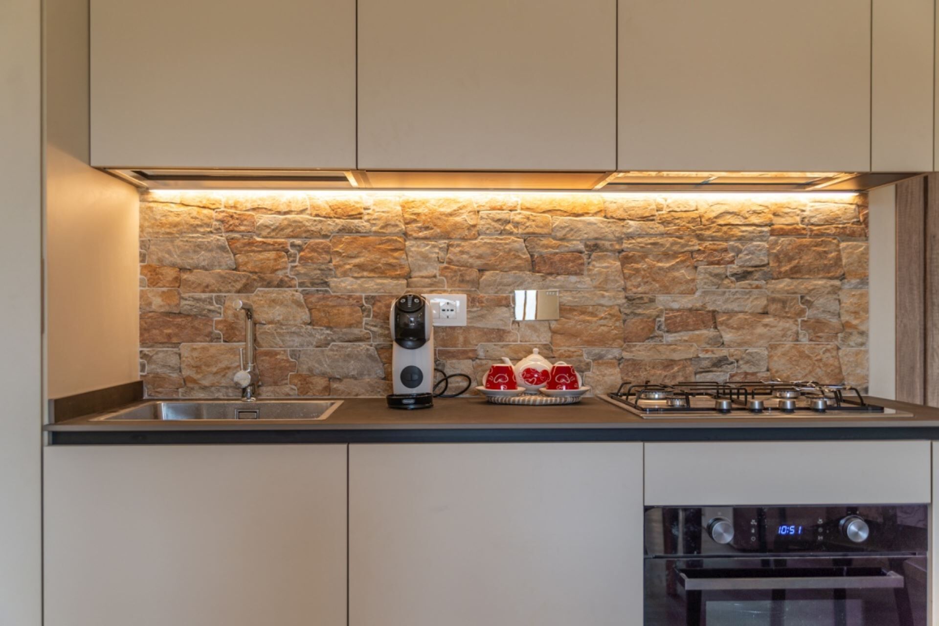 Eine Küche mit Steinrückwand, einer Kaffeemaschine, einem Gasherd und einem Backofen.