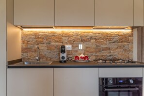 Una cocina con salpicadero de piedra, cafetera, cocina a gas y horno.