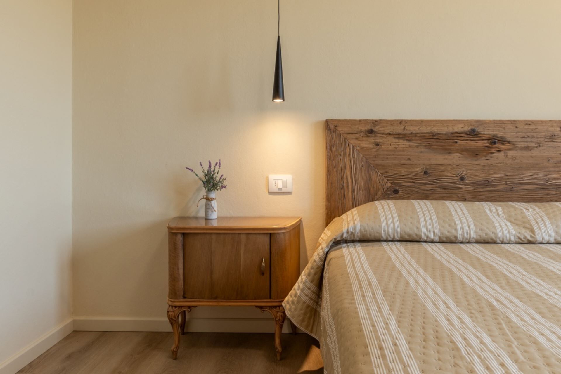 Ein Schlafzimmer mit einem Holzkopfteil, einem Nachttisch mit Blumen in einer Vase und einer Hängelampe.