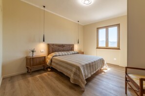 A bedroom with a wooden headboard, a bed with a striped bedspread, a nightstand with a lamp, and a window with a view. - APPARTAMENTI IL SENTIERO DEL GRANITO - GRANITO BILO 2 SX (Campo nell'Elba)