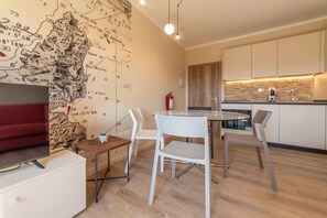 Eine moderne Küche mit Steinrückwand, ein Essbereich mit rundem Tisch und weißen Stühlen sowie ein Flachbildfernseher auf einem weißen Schrank.