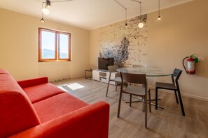 Ein modernes Wohnzimmer mit einem roten Sofa, einem Essbereich mit einem Glastisch und Stühlen, einem Fernseher und einer Karte an der Wand.
