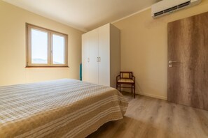 A bedroom with a bed, a wardrobe, a chair, and a wooden door. - APPARTAMENTI IL SENTIERO DEL GRANITO - GRANITO BILO 2 SX (Campo nell'Elba)