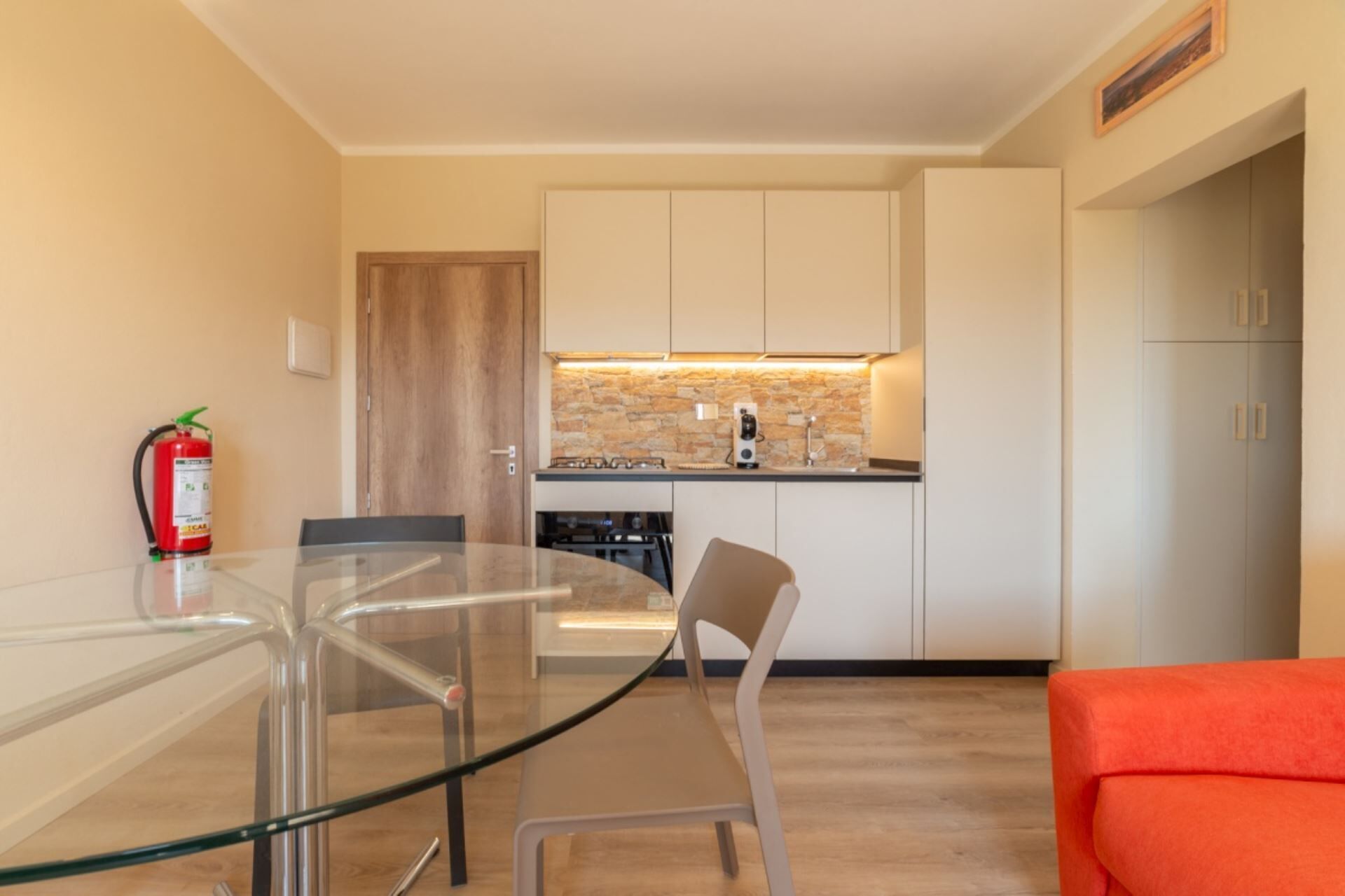 A modern kitchen with white cabinets, a stone backsplash, and a glass dining table with chairs.