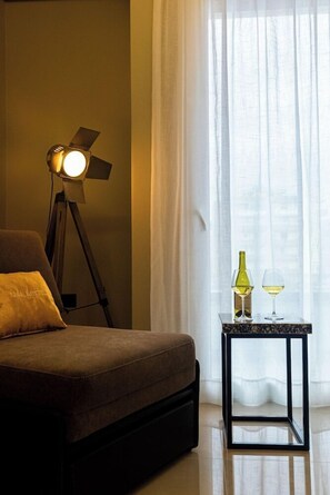 A room with a bed, a floor lamp, a table with a bottle and glass, and sheer curtains. - Kraal Hotel Vlore (Vlorë)