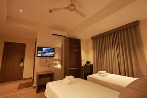 A hotel room with two beds, a television, an air conditioning unit, a ceiling fan, a wardrobe, and a window with curtains.