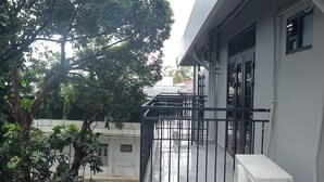 A balcony with a metal railing, a white air conditioning unit, and a tree in the background.