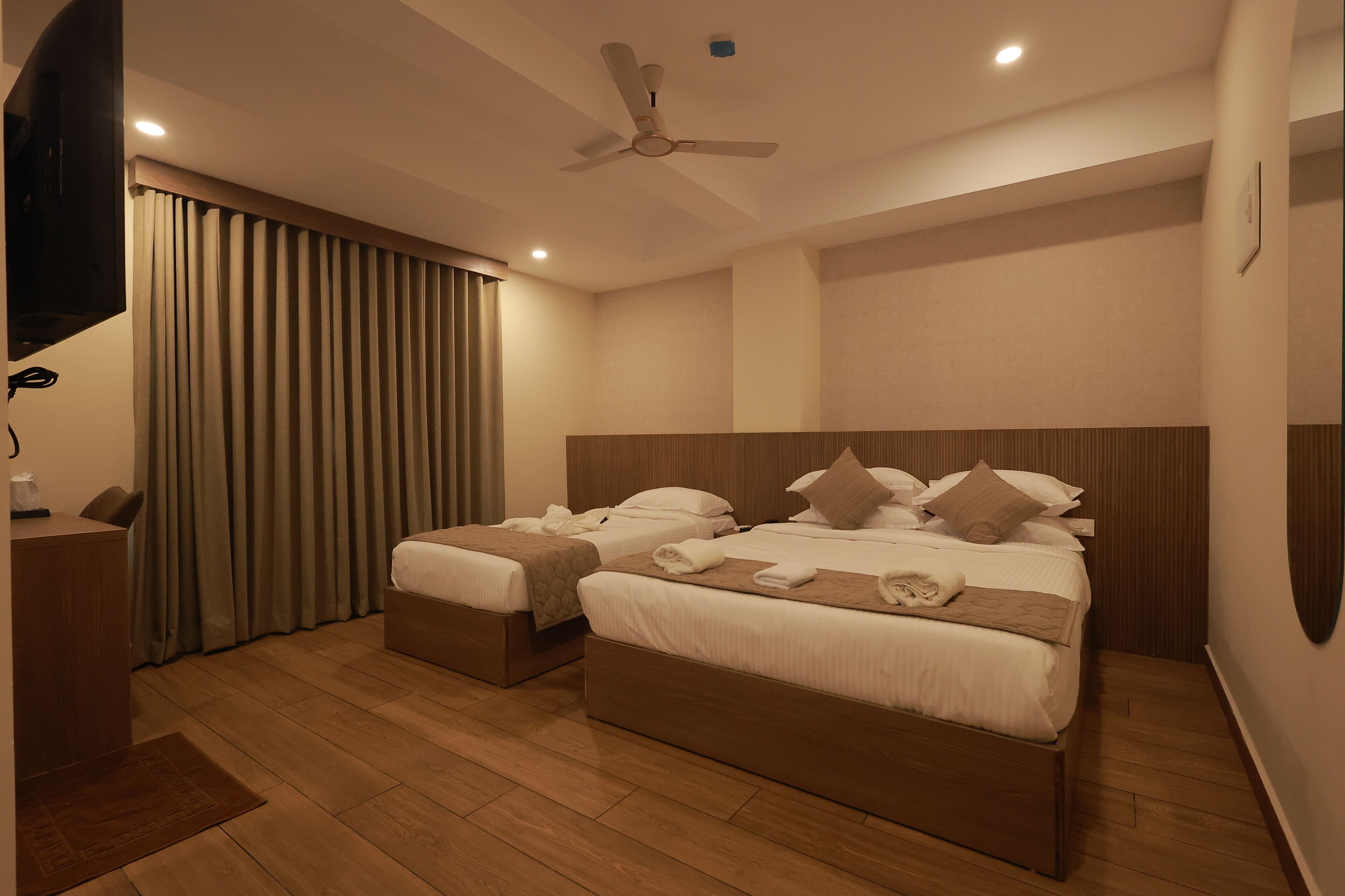 Habitación de hotel con dos camas, ventilador de techo, televisor de pantalla plana y piso de madera.