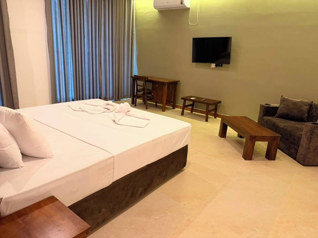 A hotel room with a bed, a desk, a chair, a sofa, and a television.