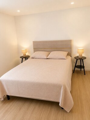 A neatly made bed with a textured bedspread and pillows, flanked by two bedside tables with lamps.