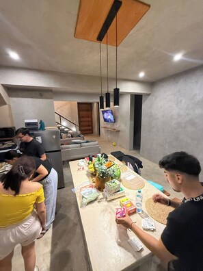 A modern kitchen with a dining area, a refrigerator, and a TV mounted on the wall.