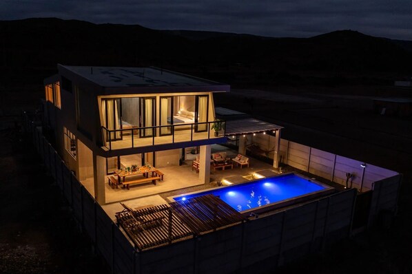A modern two-story house with a swimming pool, outdoor seating, and a covered patio area.