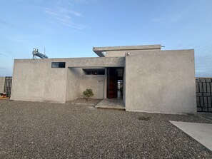 A modern building with a concrete facade, a small tree, and a gravel driveway.