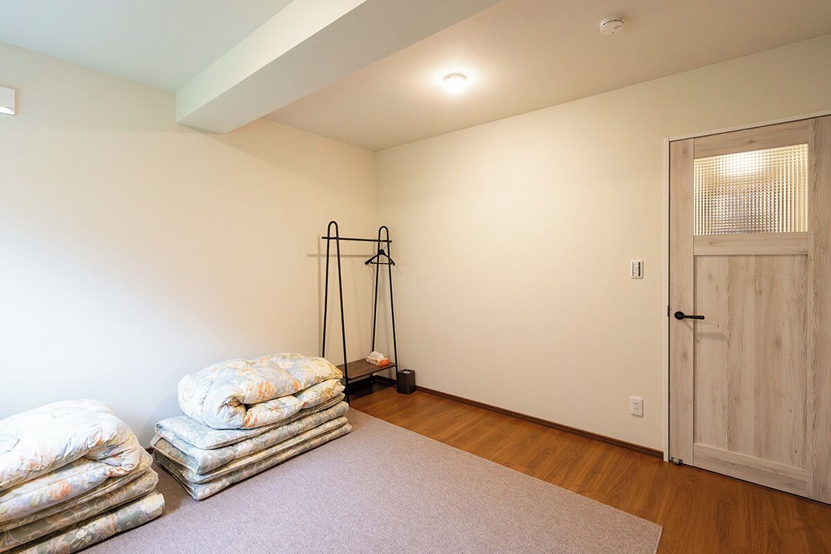 A room with a wooden floor, a door with a window, and a bed with a mattress and pillows.