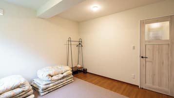 A room with a wooden floor, a door with a window, and a bed with a mattress and pillows.