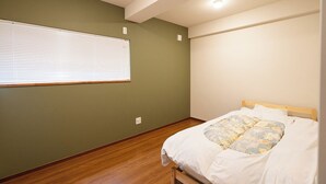 Ein Schlafzimmer mit einem Einzelbett, einem Fenster mit Jalousien und Holzboden.