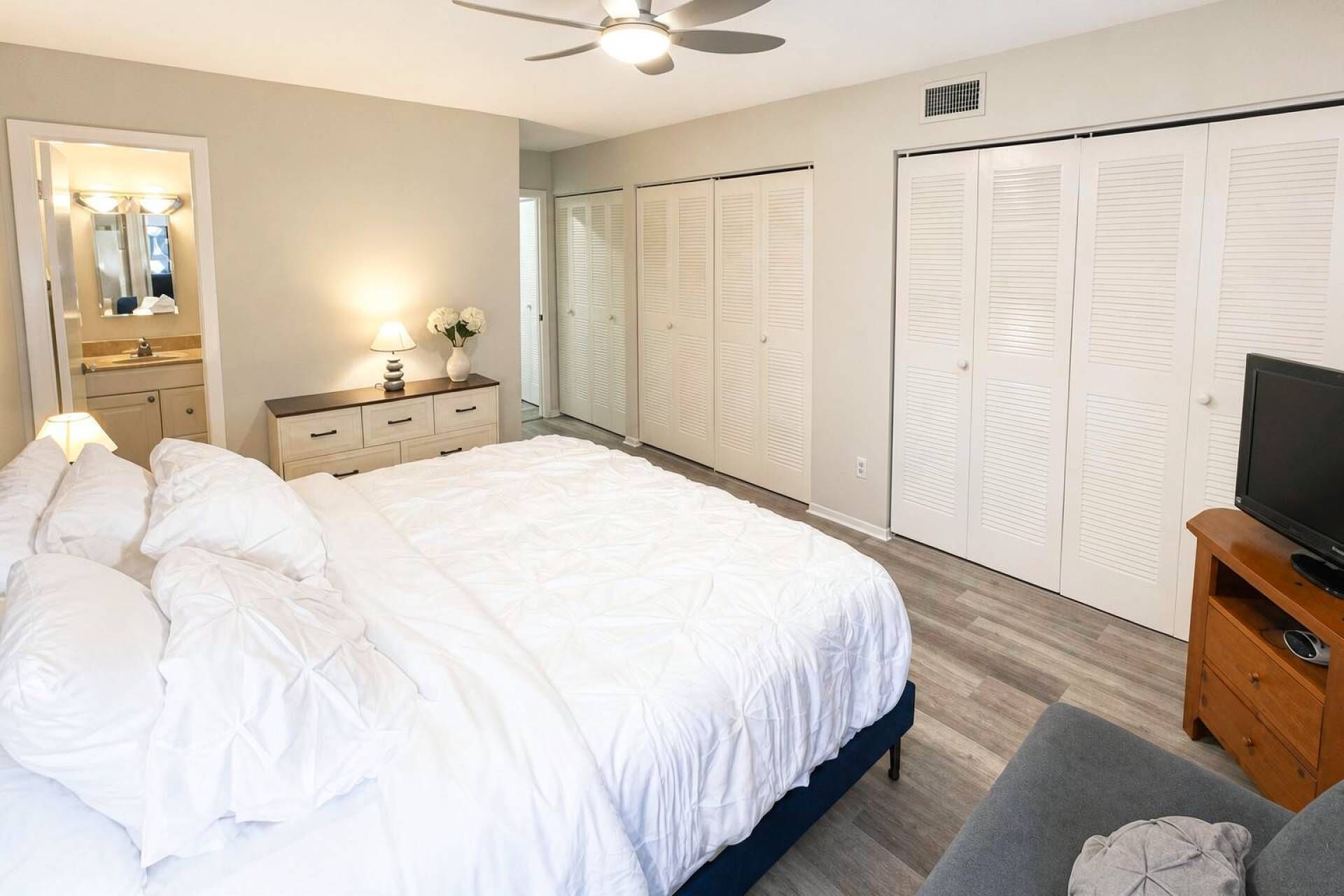 A hotel room with a bed, a dresser, a mirror, a TV, and a set of closets.