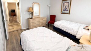 A hotel room with two beds, a dresser, a red chair, a lamp, and a framed picture on the wall. - Renovated Condo Across from Siesta Key Beach | Heated Pool | Dogs Welcome (Siesta Key)