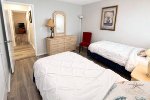 Ein Hotelzimmer mit zwei Betten, einem Schminktisch, einem roten Sessel, einer Lampe und einem gerahmten Bild an der Wand.