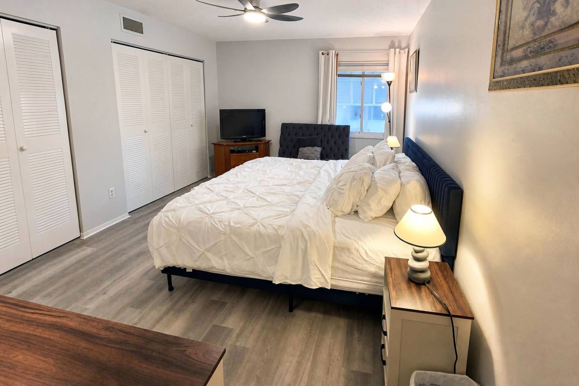 A bedroom with a bed, bedside table, lamp, TV, wardrobe, and a window with curtains.